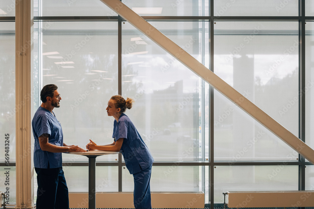 Side view of hospital staff discussing while standing by window in hospital Side view of hospital staff discussing while standing by window in hospital
