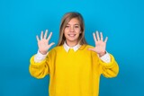 caucasian teen girl wearing yellow sweater over blue studio background showing and pointing up with fingers number ten while smiling confident and happy.