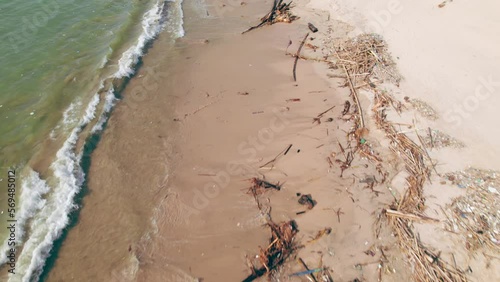 Aerial footage from drone flies over sandy ocean sandy beach, poluted with branches after storm. photo