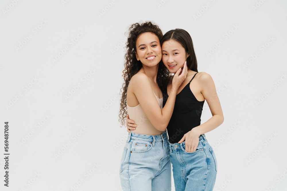 Two cheerful girls hugging while posing isolated over white wall Two cheerful girls hugging while posing isolated over white wall