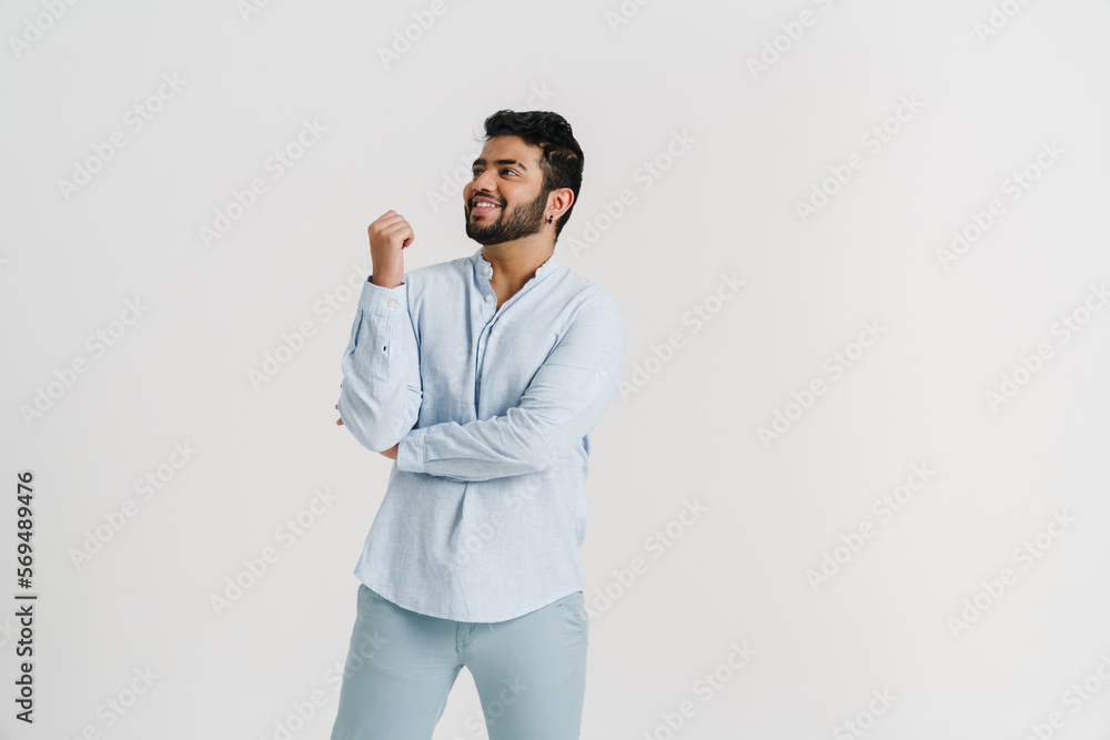 Smiling indian guy looking away while posing isolated over white wall Smiling indian guy looking away while posing isolated over white wall