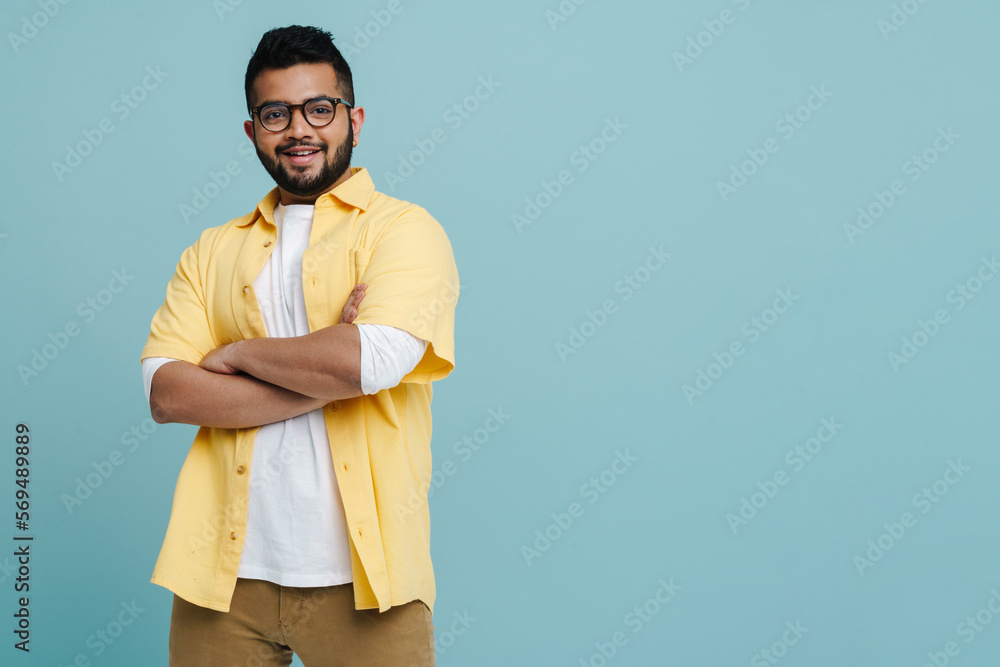 Smiling indian guy posing with arms folded isolated over blue wall Smiling indian guy posing with arms folded isolated over blue wall