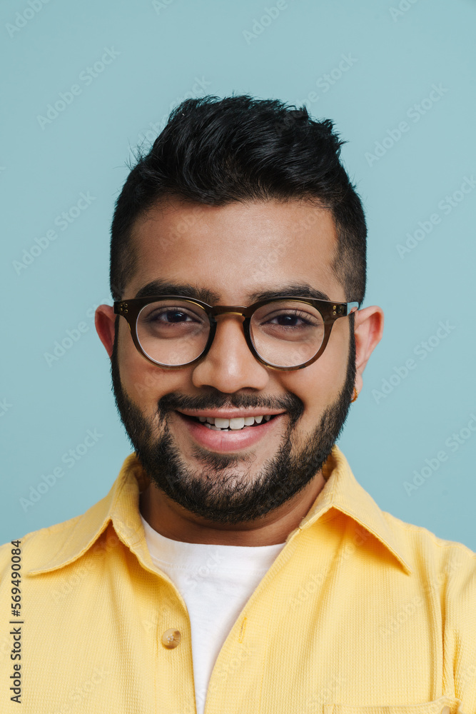 Smiling indian guy looking at camera while posing isolated over blue studio wall Smiling indian guy looking at camera while posing isolated over blue studio wall