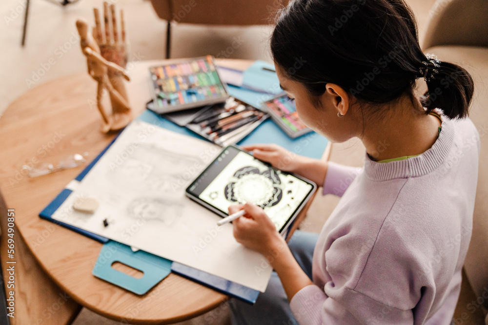 Back view of woman artist drawing on digital tablet while sitting in living room Back view of woman artist drawing on digital tablet while sitting in living room