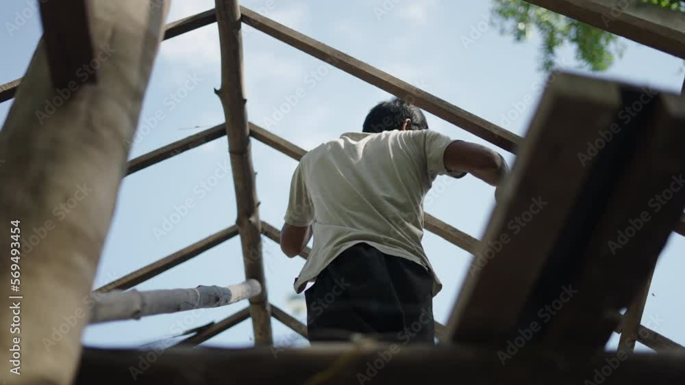 Asian man using a hammer to pin nails into a roof wood Asian man using a hammer to pin nails into a roof wood