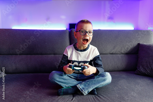 Boy Danya in glasses plays on a game console. photo