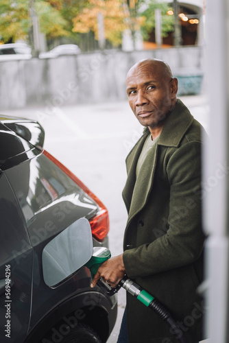 Mature man with shaved head refueling car at fuel station photo