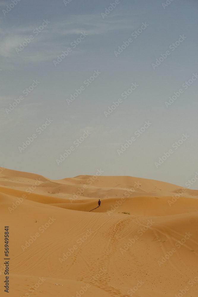 Abstract photograph of  an unrecognizable person in the middle of a sand dune shot at sunset in Merzouga, Morocco