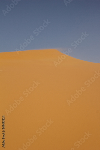 Abstract photograph of sand being blown by the wind at the top of a dune shot at sunset in Merzouga  Morocco