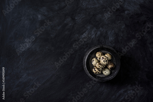 Quail eggs in a bowl on rustic black background