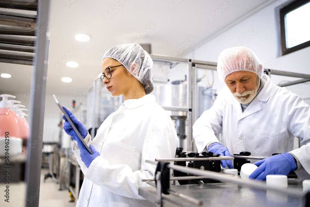 Factory workers standing by conveyor machine and controlling manufacturing of cosmetics products for pharmaceutical industry. Factory workers standing by conveyor machine and controlling manufacturing of cosmetics products for pharmaceutical industry.