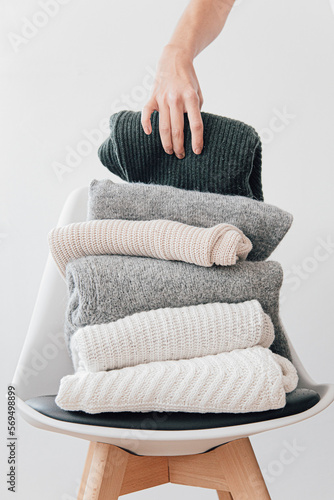 A female hand near a stack of winter wool sweaters on a chair, shot with natural window light in a studio