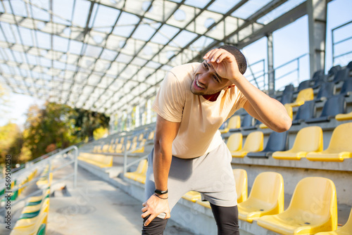 Tired hispanic athlete bent over and breathing after jogging, man doing sports on sunny day with active exercises and fitness, athlete resting after jogging. © Liubomir