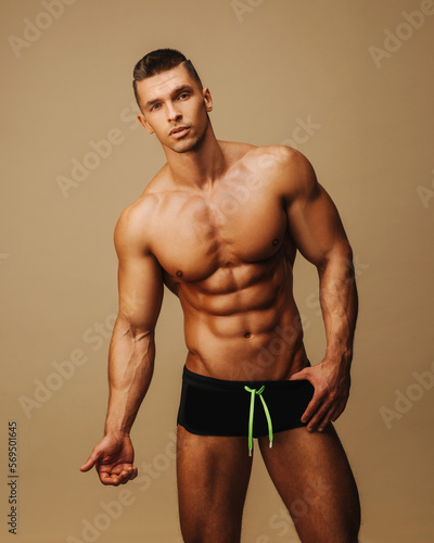 Handsome guy in swimwear posing in studio. Sexy man with six pack abs standing on neutral background. Shirtless male model in underwear. photo
