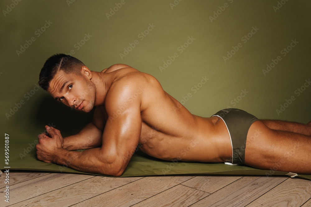 Sexy guy lying on his stomach in studio. Handsome male model posing at  green background. Muscular man in swimwear. Stock-Foto | Adobe Stock