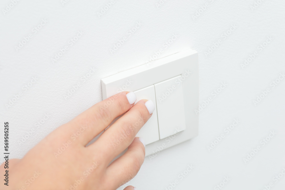 Close up of hand turning on or off light in room. Hand on wall light switcher Close up of hand turning on or off light in room. Hand on wall light switcher