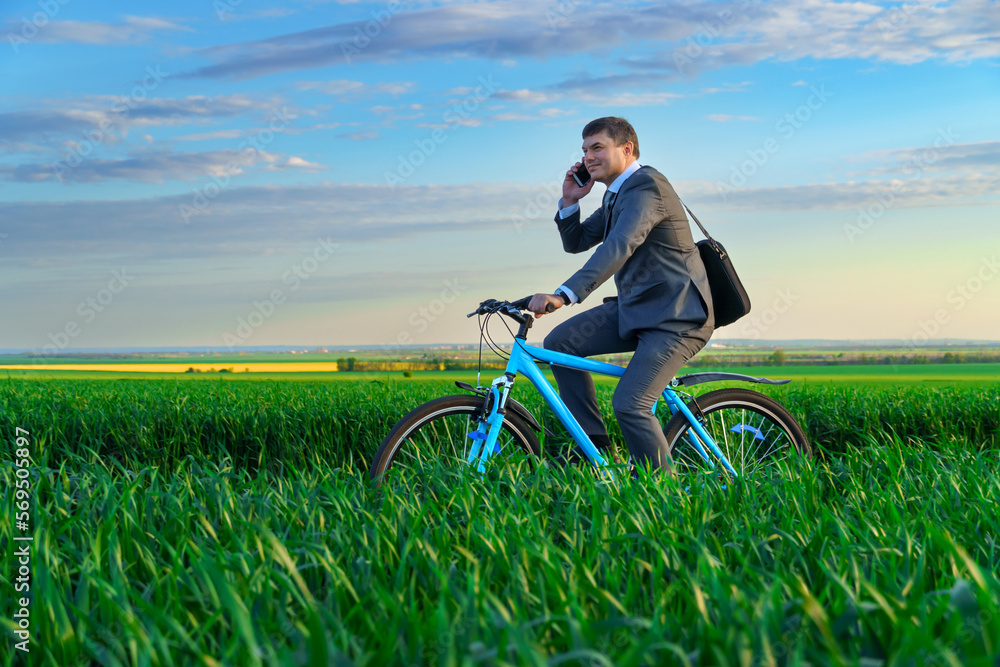 a businessman rides a bicycle on a green grassy field, dressed in a business suit, he makes a phone call, beautiful nature in spring, freelance business concept a businessman rides a bicycle on a green grassy field, dressed in a business suit, he makes a phone call, beautiful nature in spring, freelance business concept