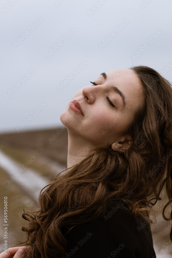 Creative portrait of a woman.Girl in a field in a cold season.Beautiful woman with long curly hair.Portrait of a beautiful girl.Emotion of calm and enjoyment.Lady in black.Vintage retro portrait.Wind.