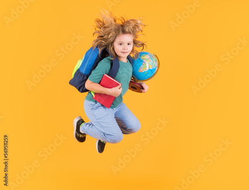 Kid jump and enjoy school. Funny excited school concept. Little student boy with backpack go to study, jumping. Schoolchild, pupil jump on yellow isolated background.