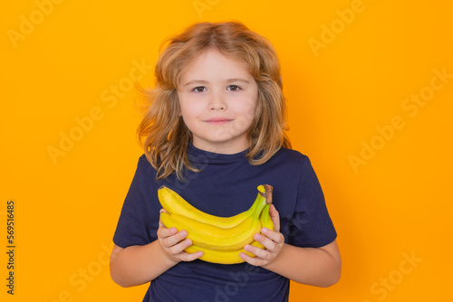 Child hold banana in studio. Studio portrait of cute kid boy with bananas isolated on yellow background, copy space.