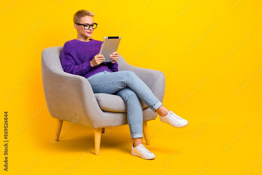 Full length portrait of positive charming person sit chair use tablet empty space ad isolated on yellow color background