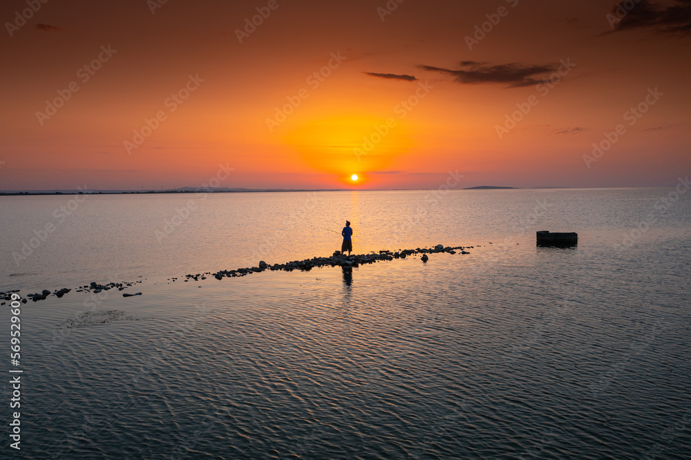 Aerial view of a fisherman on a lake during sunrise, fishing in a lake