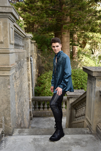 portrait of handsome brunette male model wearing fantasy medieval prince costume, romantic silk shirt. Walking around historical castle location background with stone staircase. 