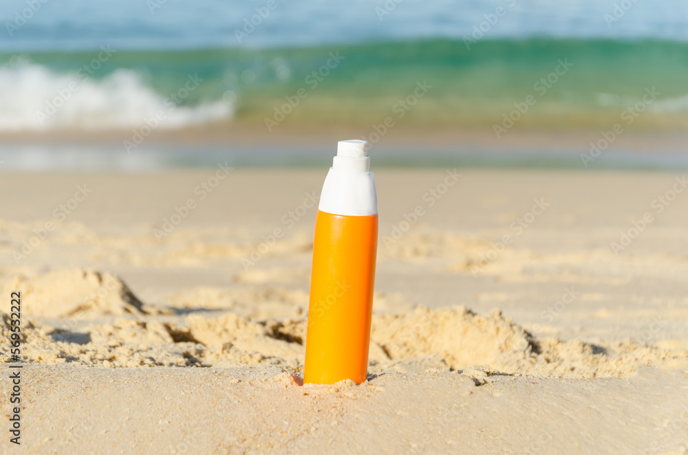 Orange bottle of sunscreen on sandy beach against backdrop of sea wave. Template, space for text