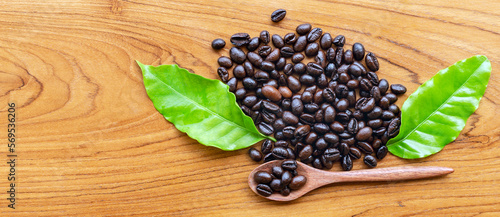 Top view of Dark roasted coffee beans and green coffee leaf on wooden background