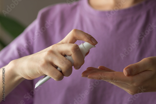 Young woman using wash hand sanitizer gel pump dispenser. Hands holds bottle of facial creame or lotion for moisturizing
