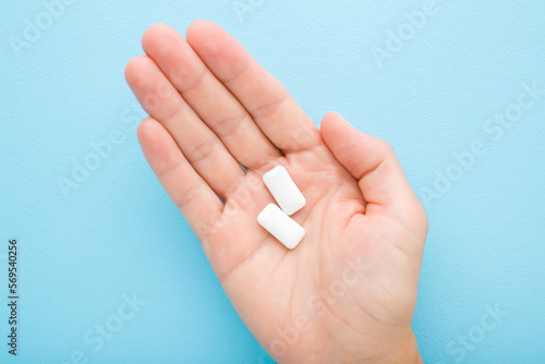 Fotografi Young adult woman palm holding and showing white chewing gum pads on light blue table background