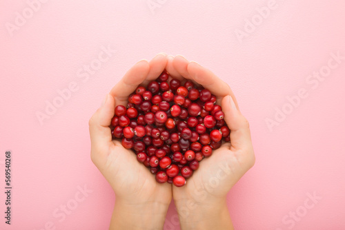 Foto Young adult woman opened palms holding heap of fresh red cranberries on light pink table background