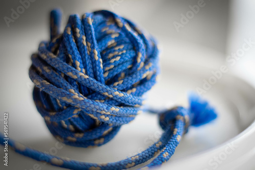 Knot of a blue polyester cord on the white plate. Blurred background. Close up view.
