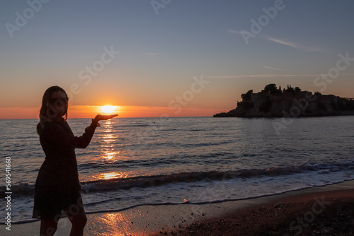 Silhouette of barefoot woman on sand beach with scenic romantic view on idyllic island Sveti Stefan at sunset, Budva Riviera, Adriatic Mediterranean Sea, Montenegro, Europe. Summer vacation at seaside © Chris