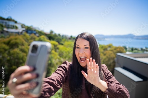 Girl video calling her friends on a zoom call. Woman on holiday skyping her family outside in a beautiful place photo