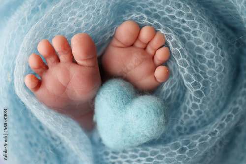 The tiny foot of a newborn baby. Soft feet of a new born in a wool blue blanket. Closeup of toes, heels and feet of a newborn. Knitted blue heart in the legs of baby. Macro studio photography. 