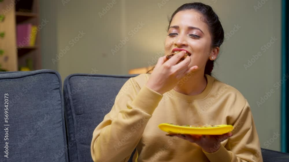 medium shot of girl enjoys eating tasty pizza by closing eyes at home on sofa - concept of yummy food, excitement and emotion or expression. medium shot of girl enjoys eating tasty pizza by closing eyes at home on sofa - concept of yummy food, excitement and emotion or expression.