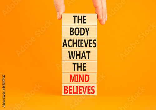 Mind and body symbol. Concept words The body achieves what the mind believes on wooden blocks. Beautiful orange background. Copy space. Businessman hand. Motivational mind and body concept. photo