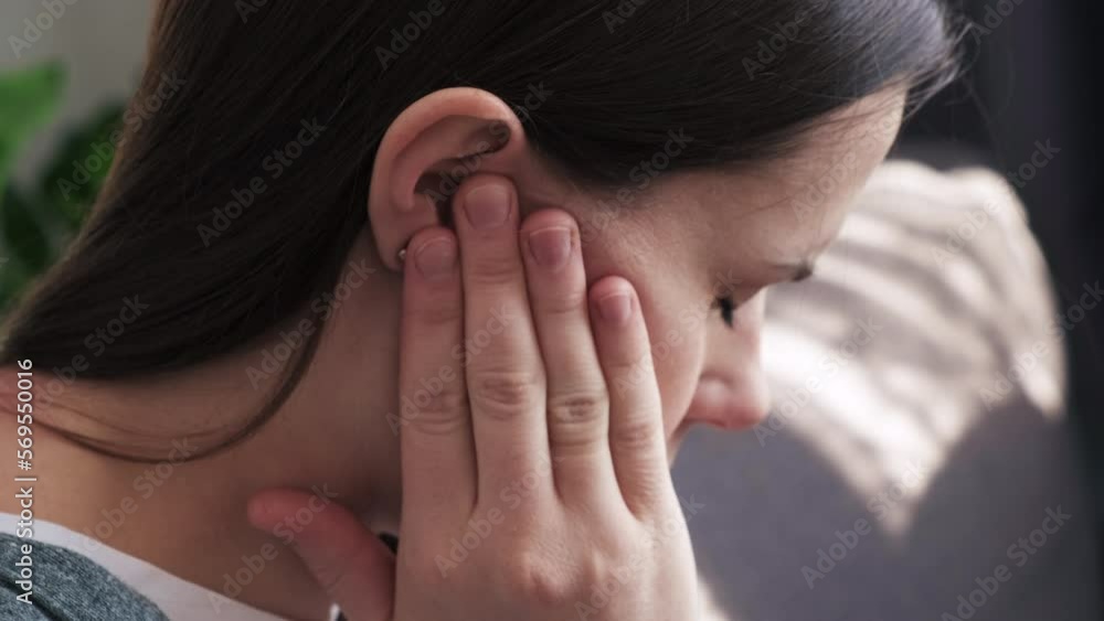 Close up of upset young brunette female holding painful ear, suddenly feeling strong ache. Unhealthy caucasian woman suffering from painful otitis sitting on sofa at home. Health problems concept Close up of upset young brunette female holding painful ear, suddenly feeling strong ache. Unhealthy caucasian woman suffering from painful otitis sitting on sofa at home. Health problems concept