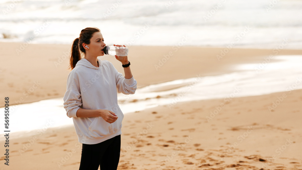 Sport and hydration. Young fit woman drinking mineral water from bottle, resting after training by seaside, copy space Sport and hydration. Young fit woman drinking mineral water from bottle, resting after training by seaside, copy space