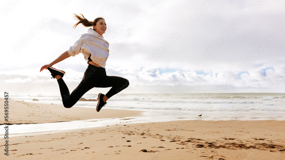 Young fit lady jumping high on beach ocean, active european woman working out outdoors, panorama with copy space
