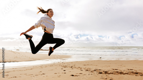 Fototapeta Naklejka Na Ścianę i Meble -  Young fit lady jumping high on beach ocean, active european woman working out outdoors, panorama with copy space