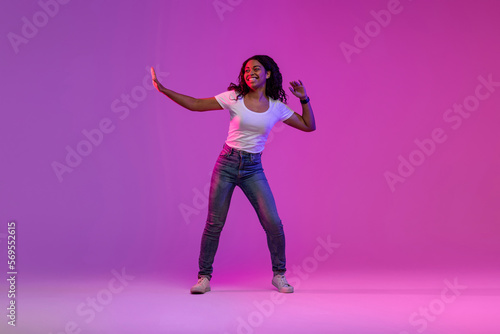 Carefree Young Black Woman Dancing In Neon Light Over Gradient Purple Background