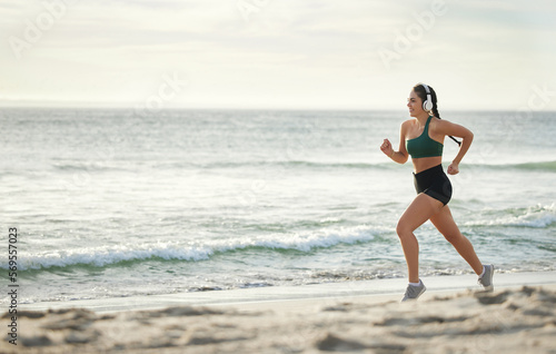 Woman listening to music, running on beach and morning cardio routine for healthy lifestyle in California. Fitness workout by sea, young athlete with headphones and sports exercise in summer mockup