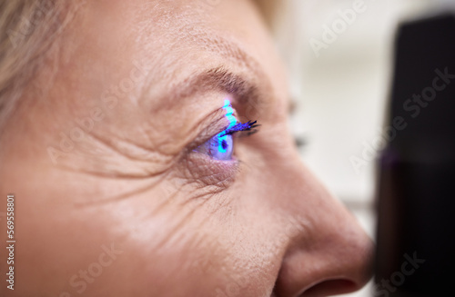 Eye exam, vision or laser test for an old woman with a machine at optometry consultation for retina problem. Senior, patient or client with medical health insurance checking eyesight at optician photo