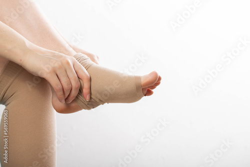 Pregnant girl puts on compression stockings for varicose veins on her legs. White background. Pregnancy and varicose veins, phlebology. photo