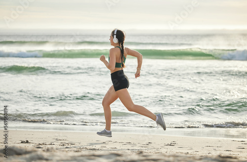 Woman running on beach, listening to music and morning cardio routine for healthy lifestyle in California. Fitness workout by sea, young athlete with headphones and sports exercise in summer