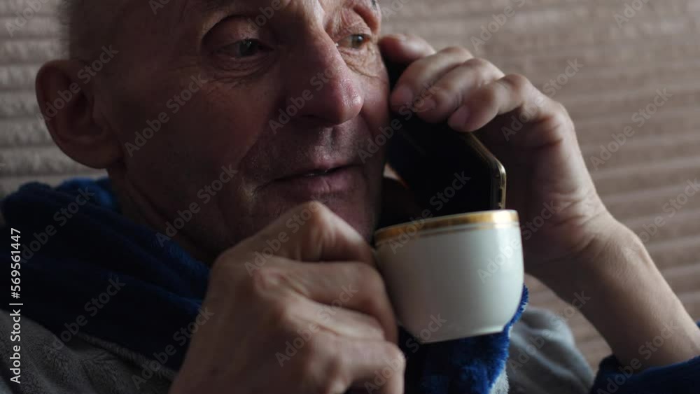 caucasian active pensioner 70 years old in a bathrobe sitting on the couch cheerfully talking on the phone and drinking coffee from a cup .elderly people talking on the phone. caucasian active pensioner 70 years old in a bathrobe sitting on the couch cheerfully talking on the phone and drinking coffee from a cup .elderly people talking on the phone.