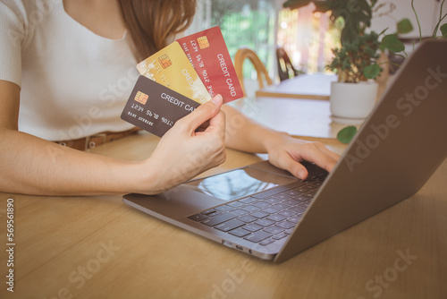 Close up female hand holding credit card and choosing to use. Young woman using computer laptop for digital banking, internet payment, online shopping, financial technology, E-commerce concept.