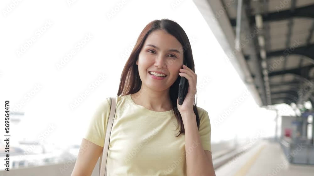 Portrait of beautiful smiling Asian woman standing on platform waiting for electric train in the morning and holding a smartphone. The concept of traffic and capital transportation Portrait of beautiful smiling Asian woman standing on platform waiting for electric train in the morning and holding a smartphone. The concept of traffic and capital transportation